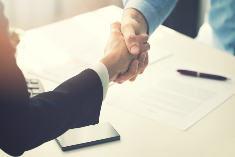 Two business professionals shaking hands over business documents