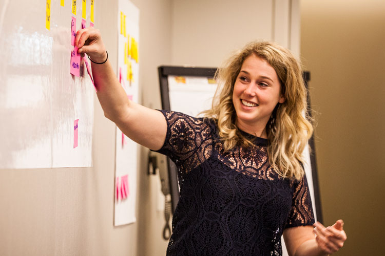 Female at white board adjusting process mapping sticky notes.